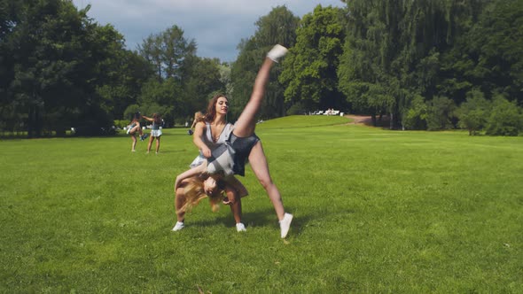 Cheerleader Helping Friend Doing Cartwheel and Sharing High-five Training Outdoors