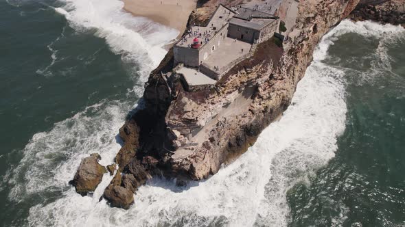 Ocean waves crashing on Nazaré lighthouse cliff, Portugal. Aerial top-down circling