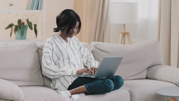 Young Woman Sitting on Comfortable Sofa in Living Room Typing on Laptop Female Freelancer Working