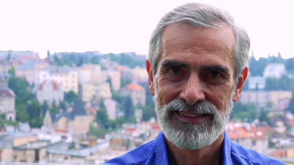 Old Senior Man Smiles To Camera - City (Buildings) in Background - Closeup