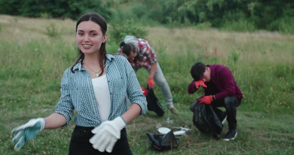 Happy Girl Crosses Hands Smiles at Camera at People Collecting Garbage