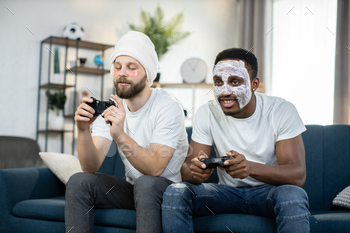 Multiethnic men doing skin care procedures, playing video games using joysticks