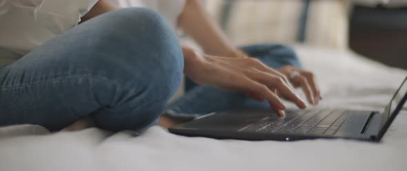 Woman hands typing something on a laptop keyboard in the bedroom. 