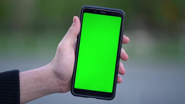 Man Holding Mockup Smartphone with Green Screen Outdoors on the Street