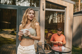 Pretty long-haired blonde woman with a coffee cup standing outsie the cottage - PhotoDune Item for Sale