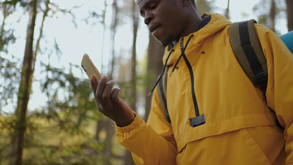 A Black Man Walks Through the Forest with the Phone and Looks at the Navigation Application