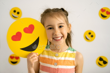 day Party. Emotions. A little girl, smiling with all her teeth, holds a cardboard love emoji in her hands.