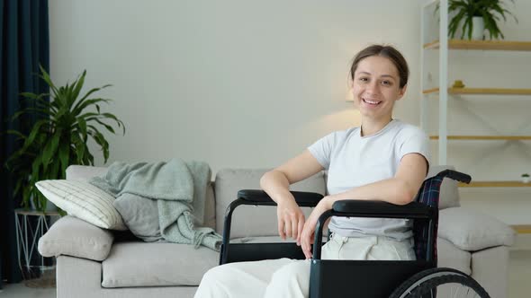 Portrait of Young Woman Sitting in Wheelchair at Home and Looking at Camera with Smile