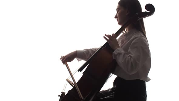 Silhouette of woman sitting and playing the cello on white background, side view. Studio