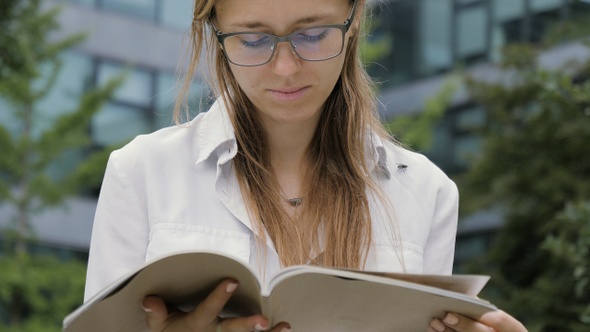 A Young Blonde Woman Outdoors in Park with A Magazine.