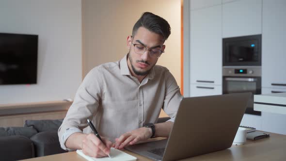 Young Indian Student at Home Office Watching Webinar Using Laptop Making Notes