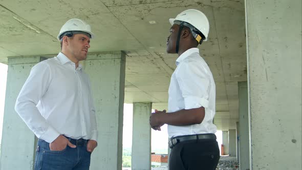 Handsome Construction Businessmans in Protective Helmets and Vests Are Shaking Hands at Construction