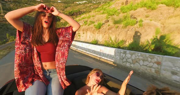 Beautiful brunette sitting on hood of convertible riding with her friends