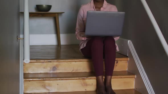 African american woman using laptop while sitting on stairs working from home