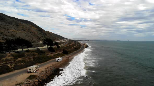 Aerial drone shot low over the ocean waves next to RV campers and the cliffs along the 101 freeway i