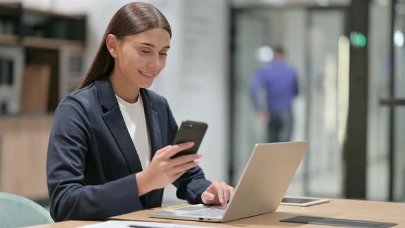 Disappointed Businesswoman Using Smartphone and Laptop in Office 