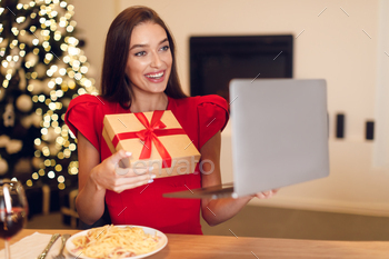 ating. Portrait of beautiful young woman holding laptop computer in hands and showing gift box to web camera during video chat with partner