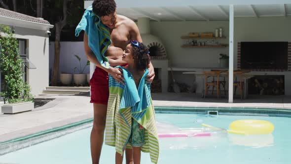 Happy biracial man and his son standing by swimming pool in garden