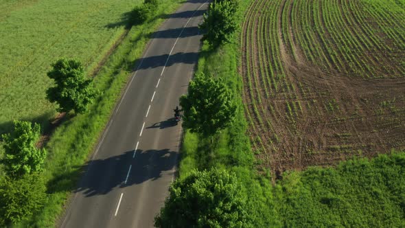 Motorbiker Rides on Road Approaching Cars Aerial View