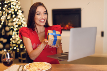 holiday online, holding gift box during video call with friend or family, sitting at table with laptop computer at home. Distance party celebration