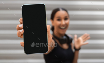 With Blank Black Screen At Camera While Standing Outdoors, Cheerful Young Woman Advertising Fitness Application Or Website, Selective Focus, Mockup
