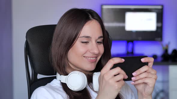 Cute Gamer Woman Sit on a Gaming Chair Smiling and Playing Mobile Online Game on a Smartphone