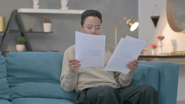 African Woman Reading Documents on Sofa