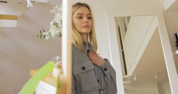 Blonde Woman Trying On The Grey Jacket With Belt In Front Of The Mirror