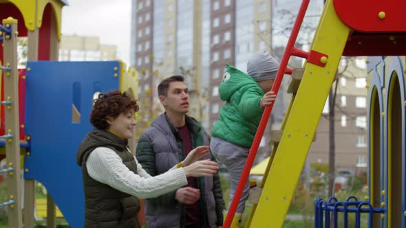 Young Boy Climbing up Ladder at Playground and Parents Guarding alt