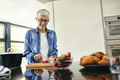 Senior woman standing in kitchen, chopping strawberries - PhotoDune Item for Sale
