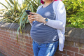 Pregnant woman typing on her phone outside - PhotoDune Item for Sale