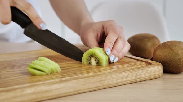 Woman Cut the Kiwi on a Wooden Board in the Kitchen