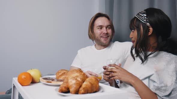 Young Multiracial Couple Relaxing in the Bedroom and Eating Breakfast in Bed