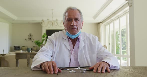 Portrait of caucasian senior male doctor with lowered face mask talking looking at the camera