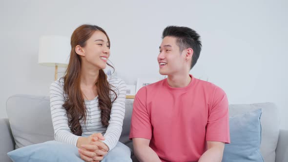 Portrait of Asian young loving couple sitting on sofa in living room.