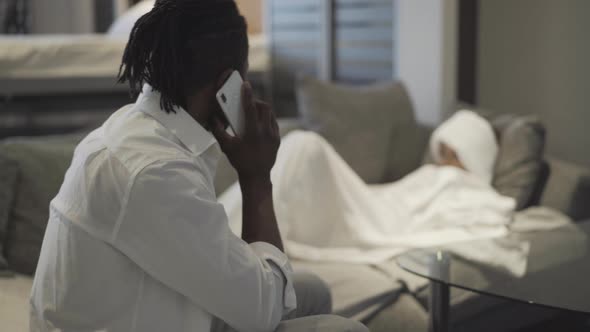 Anxious African American Man Talking Phone Blurred Ill Girl Lying Background