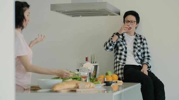 Homosexual Married Lesbian Couple Relaxing with Glasss of Alcohol Wine in Kitchen While Cook Rbbro