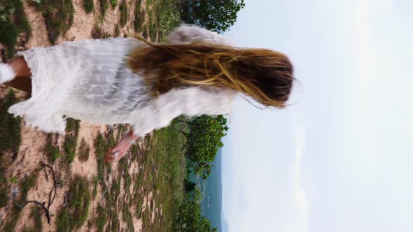 An attractive woman with long healthy hair running towards spectacular nature view. Vertical video.