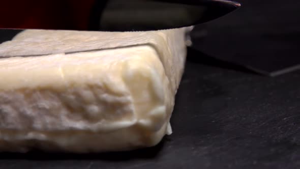 Knife Cuts a Soft Cheese on a Black Board