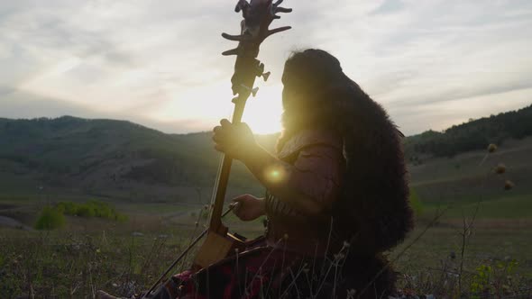 Folk Musician Plays Tovshuur with Bow in Mountain Valley