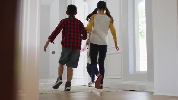 Excited asian son and daughter at home running to greet parents coming through the front door