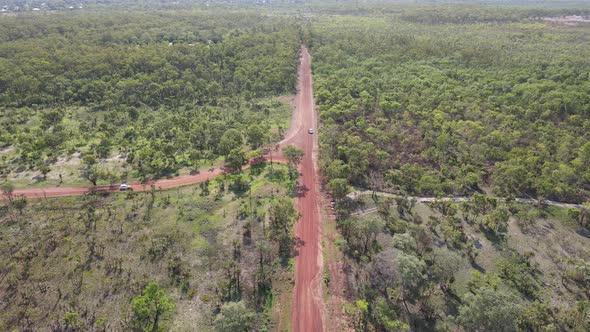 High Slow moving drone shot of Car driving meeting a Long Red Road and Green Bushland near Holmes Ju