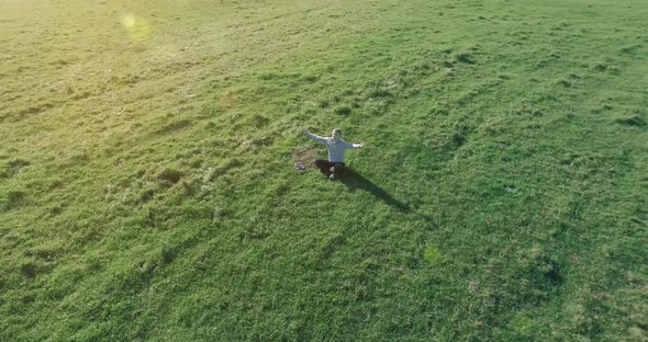 Low Orbital Flight Around Man on Green Grass with Notebook Pad at Yellow Rural Field.