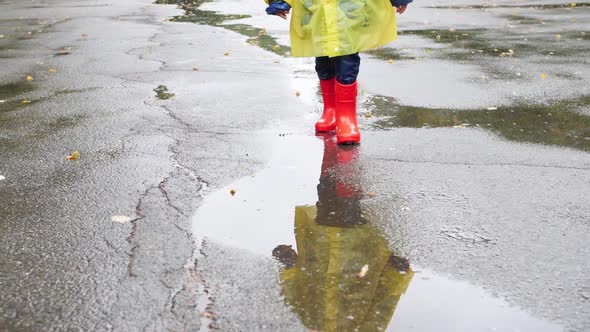 Slow Motion Video of Little Boy in Red Wellington Boots and Yellow Raincoat Walking Over Big Puddles