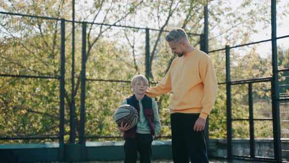 Dad Puts His Arm Around His Son While Talking at Basketball Court on a Sunny Day