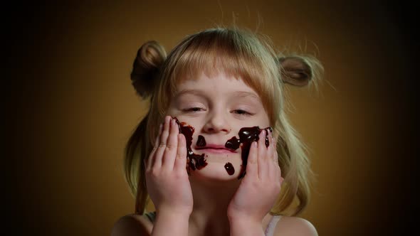 Portrait of Teen Smiling Child Kid Girl Smears Face with Melted Chocolate and Showing Thumbs Up Sign