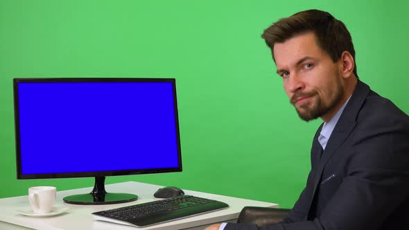 A Young Businessman Sits in Front of a Computer and Shows a Thumb Down To the Camera - Green Screen