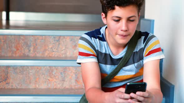 Schoolboy sitting on staircase and using mobile phone