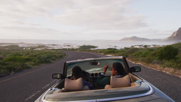 Rear view of diverse couple driving on sunny day in convertible car raising their arms in the air