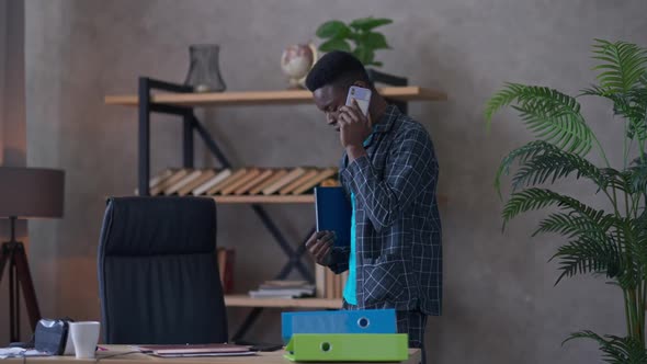 Concentrated Man in Pajamas Talking on the Phone Walking to Table in Living Room Sitting Down on